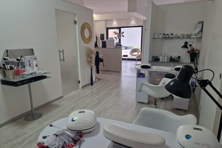 Receção e zona de manicure em Estetica Francesca em Olbia com espelho redondo na parede e prateleiras de vidro com produtos de beleza.