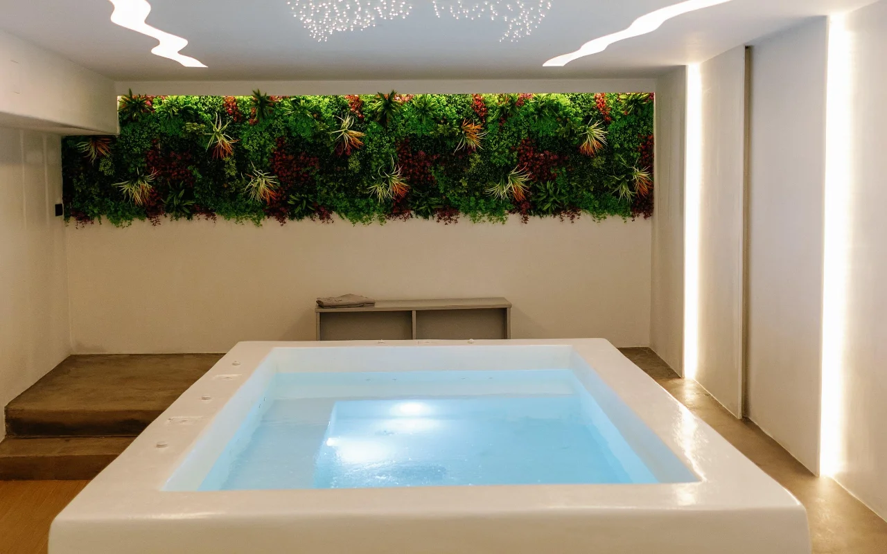 A piscina de hidroterapia do Liana Spa Therapy em Naxos, suavemente iluminada por dentro, sob uma parede verde colorida de plantas preservadas e um teto salpicado de minúsculas luzes-estrela.