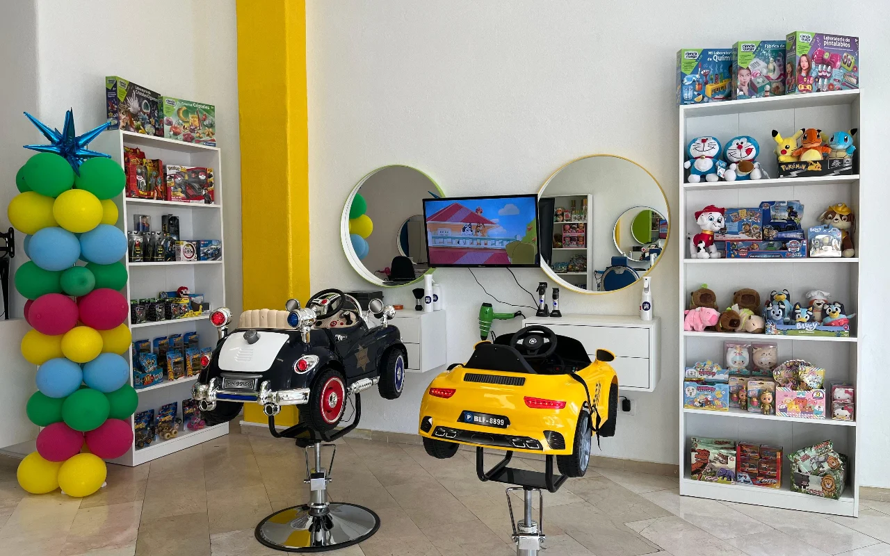 A zona infantil da Peluplay em Benalmádena, onde as cadeiras de styling têm a forma de carrinhos de brincar, com prateleiras cheias de personagens de desenhos animados, espelhos redondos e uma coluna de balões.