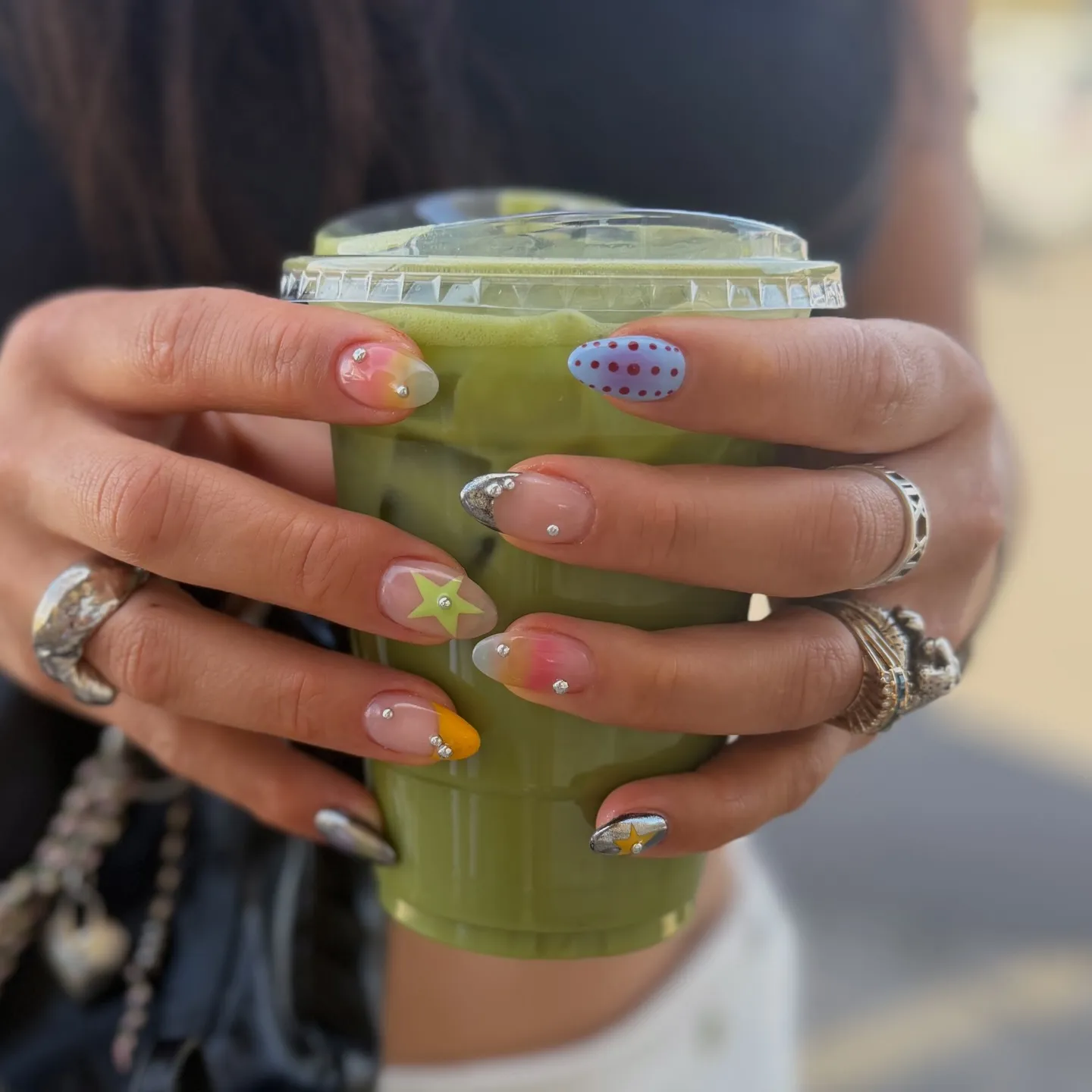 Conjunto variado de nail art com pequenos piercings de cristal, motivos de estrela e apontamentos de cor em unhas em formato amêndoa