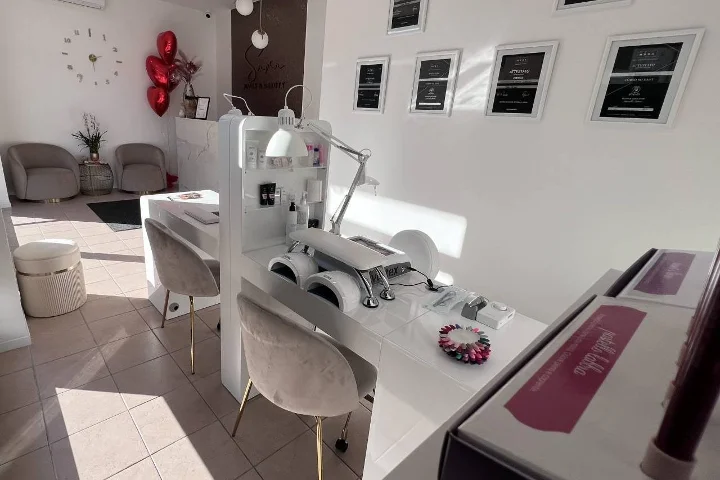 Salão de unhas branco Sara Nails&Beauty em Tortolì com cadeiras de veludo cinzento e certificados emoldurados na parede.