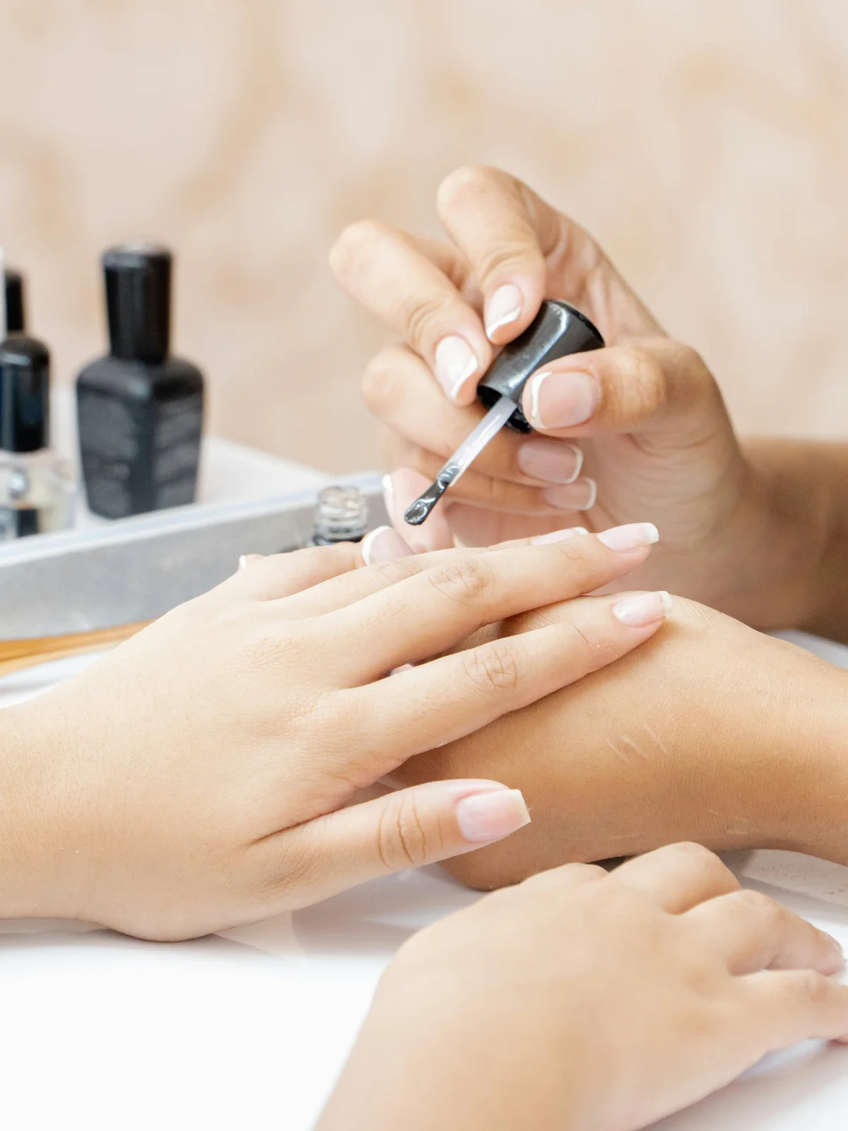 Grande plano de uma manicure profissional a aplicar um tratamento reforçante transparente nas unhas de uma cliente no salão