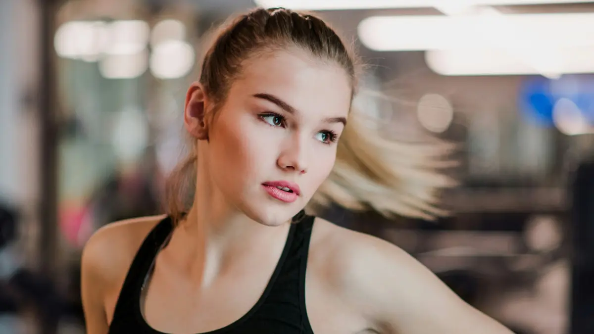 Uma jovem de top desportivo move-se para o lado enquanto o cabelo apanhado lhe voa para fora