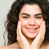 Uma jovem de pele limpa e cabelo escuro ondulado sorri para a câmara