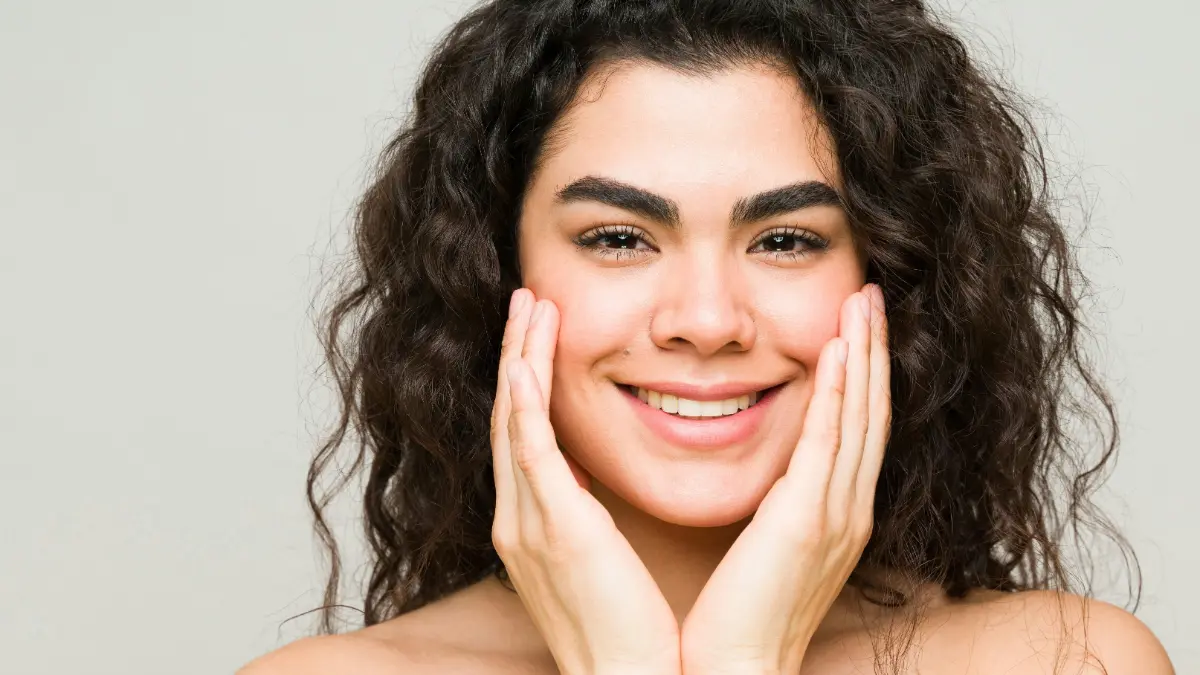 Uma jovem de pele limpa e cabelo escuro ondulado sorri para a câmara