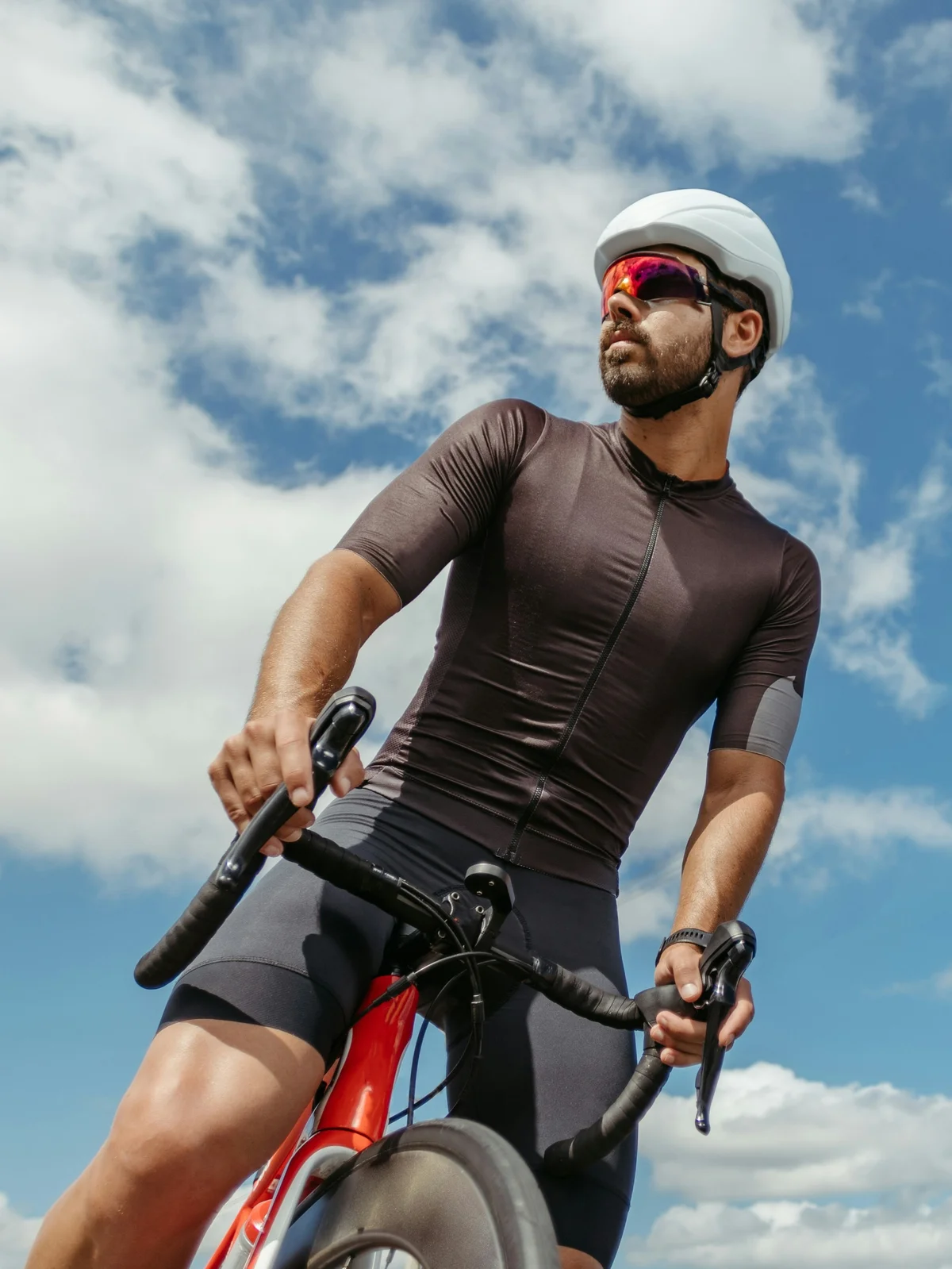Fotografado de baixo, um ciclista escarranchado na bicicleta pára para olhar em redor sob um céu azul com nuvens