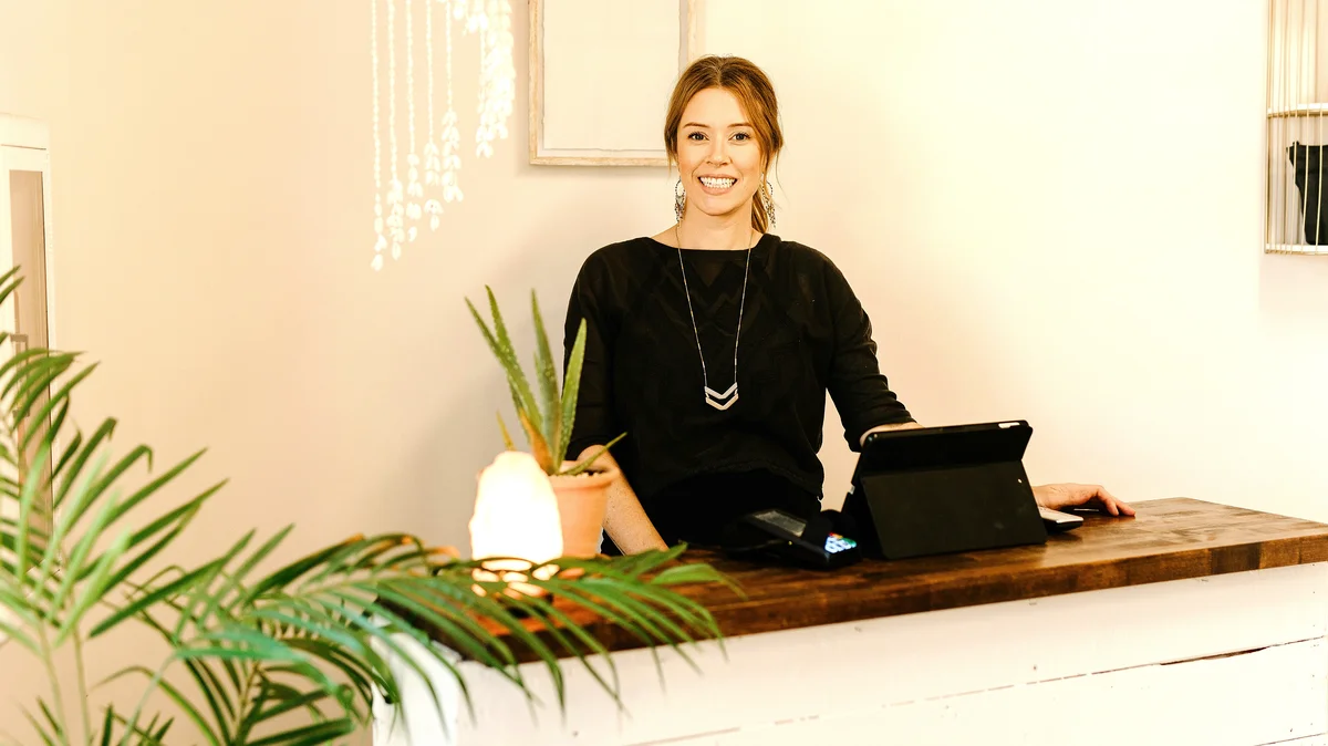 Uma mulher sorridente está atrás do balcão de receção de um centro de estética
