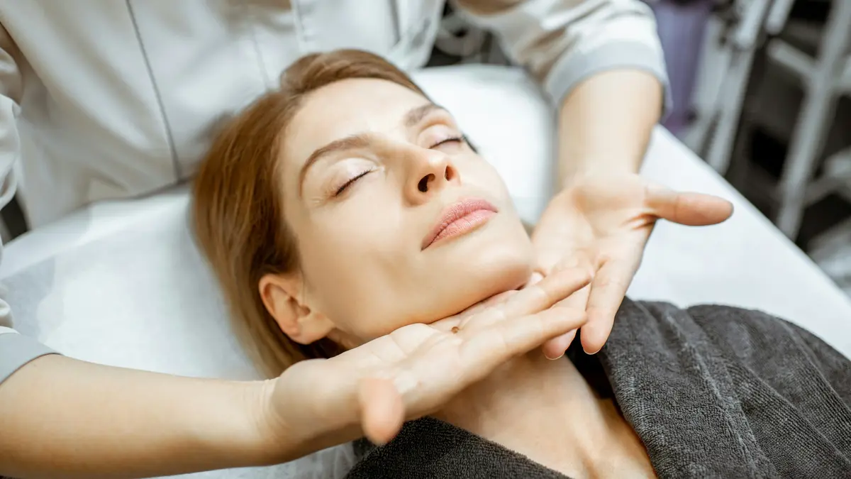 Mulher relaxada durante uma massagem suave de drenagem linfática ao rosto, com as mãos da profissional a deslizar levemente sob o maxilar